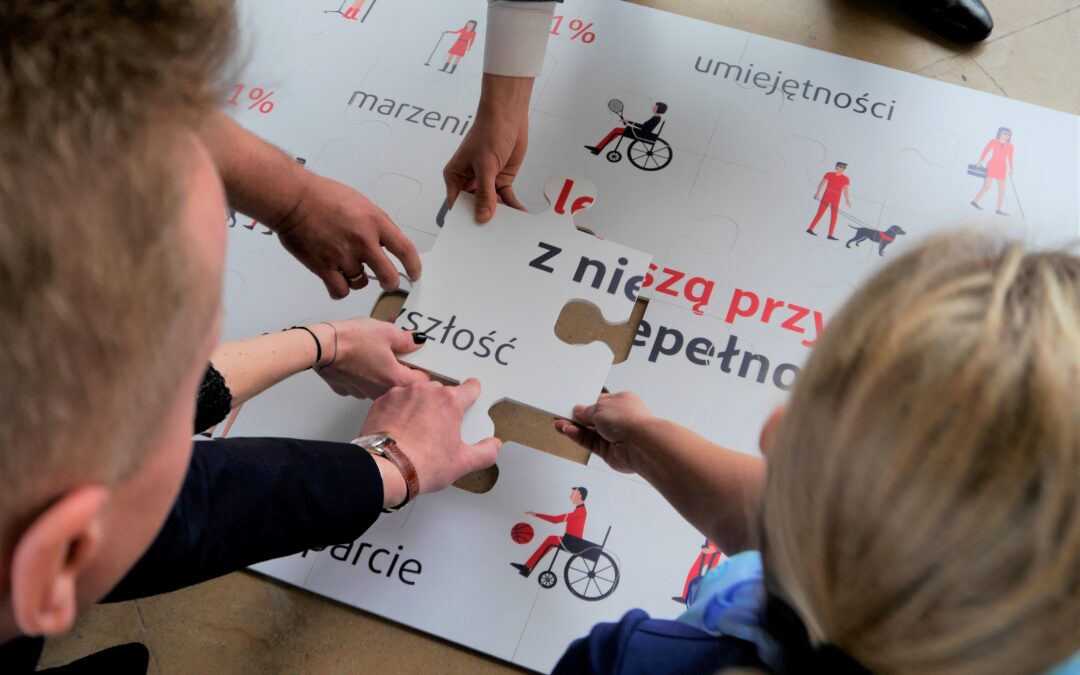 Osoby na zdjęciu układają wielkie puzzle, z hasłem ułóż przyszłość z niepełnosprawnością
