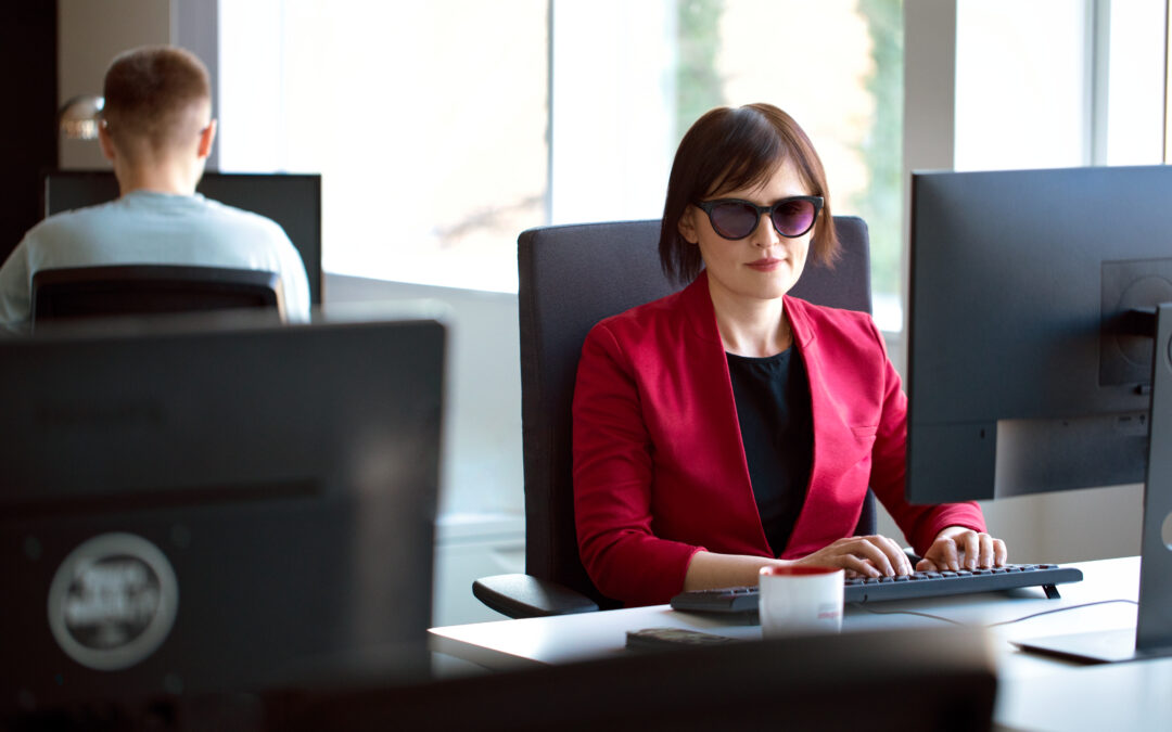Kobieta w ciemnych okularach siedzi przy komputerze.